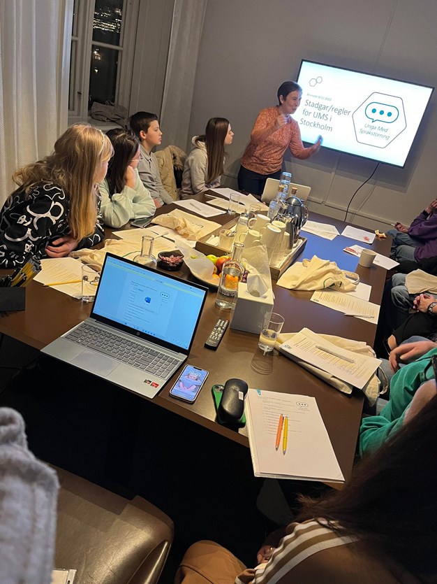 Möte med lokalföreningen UMS i Stockholm. Man ser ett antal ungdomar runt ett bord och en person som visar en presentation